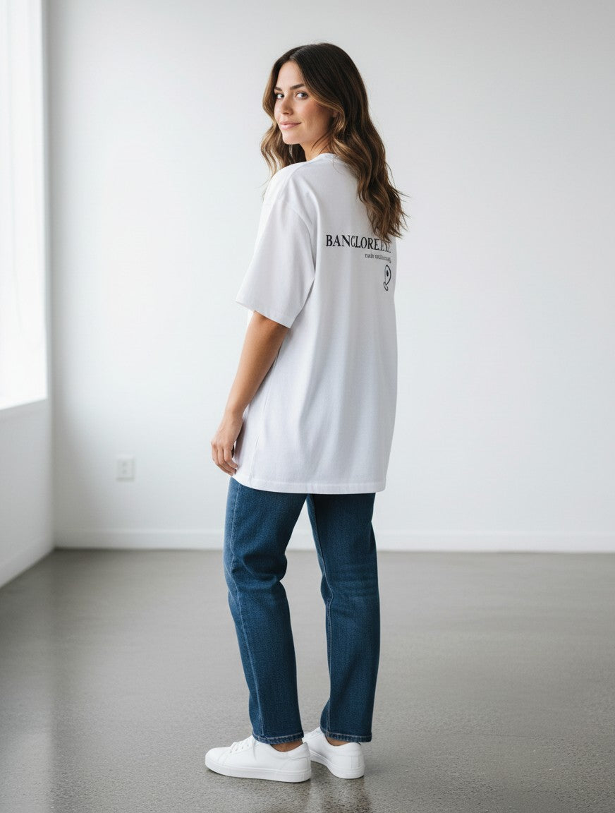 A woman wearing a white mi-DONE oversized cotton Bengaluru t-shirt with drop shoulders and back graphic print.
