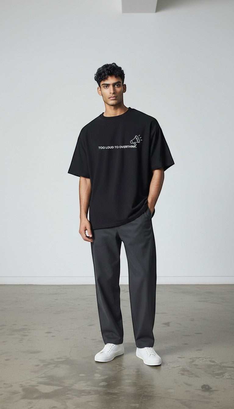 A male model wearing a black mi-DONE oversized cotton t-shirt with Too Loud To Overthink graphic print and drop shoulders