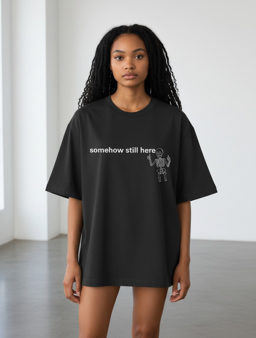 Model wearing a black mi-DONE oversized cotton t-shirt with a white skeleton graphic and text somehow still here