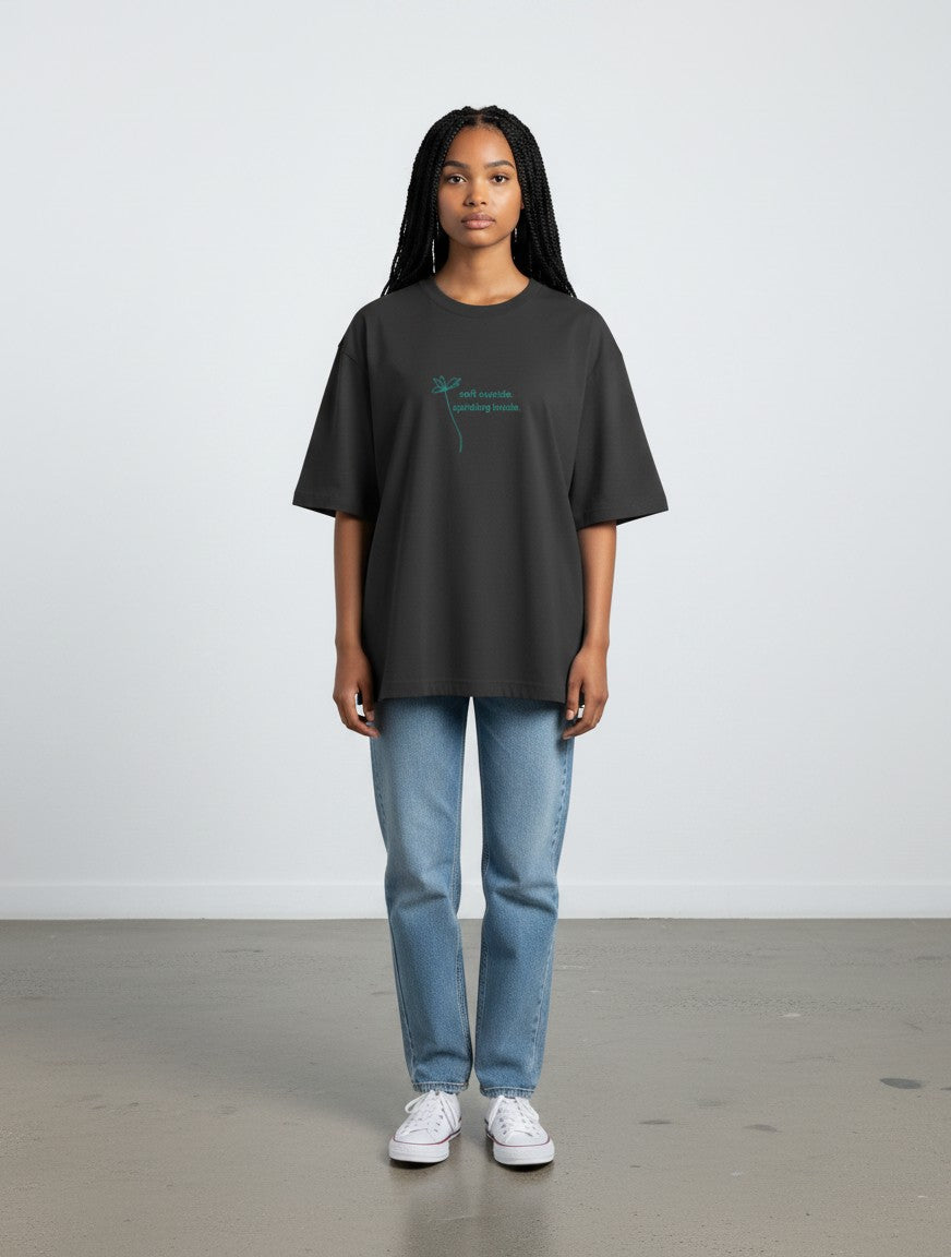 Model wearing a charcoal grey mi-DONE oversized cotton t-shirt with a small teal flower graphic and text on the chest.