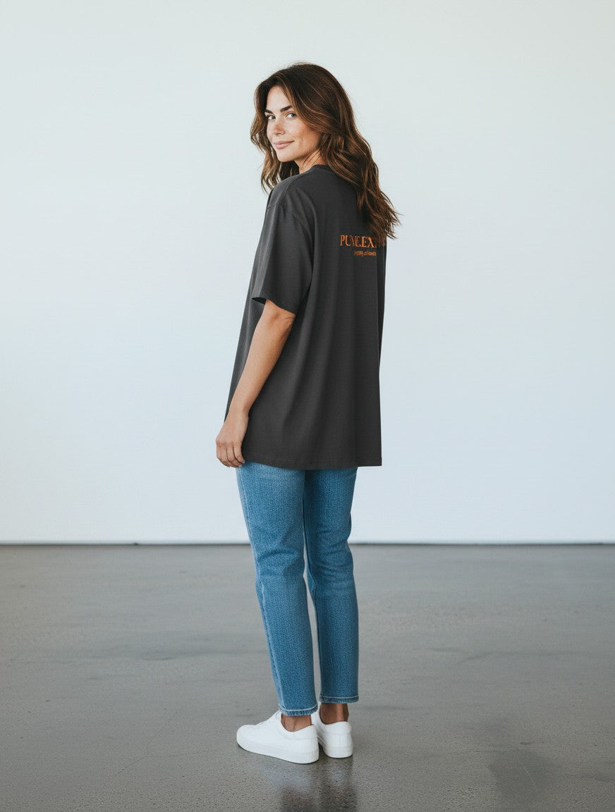 Woman wearing a charcoal grey mi-DONE oversized cotton t-shirt with Pune print, paired with blue jeans and white sneakers