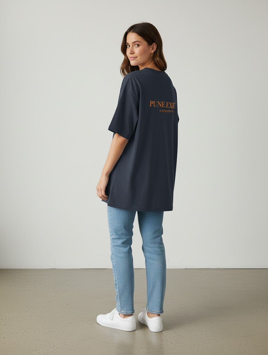 A woman wearing a charcoal grey mi-DONE oversized cotton t-shirt with Pune graphic print, paired with blue jeans.
