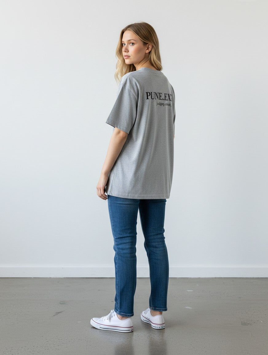 Woman wearing a grey mi-DONE oversized cotton t-shirt with PUNE.EXT print on the back, paired with blue jeans.