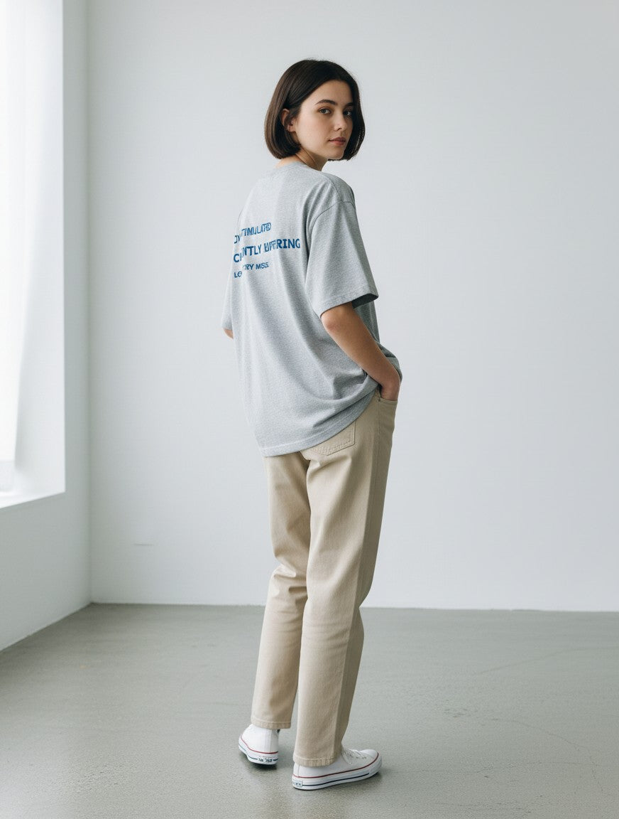 Woman wearing a grey mi-DONE oversized cotton t-shirt with blue back print, paired with beige trousers.