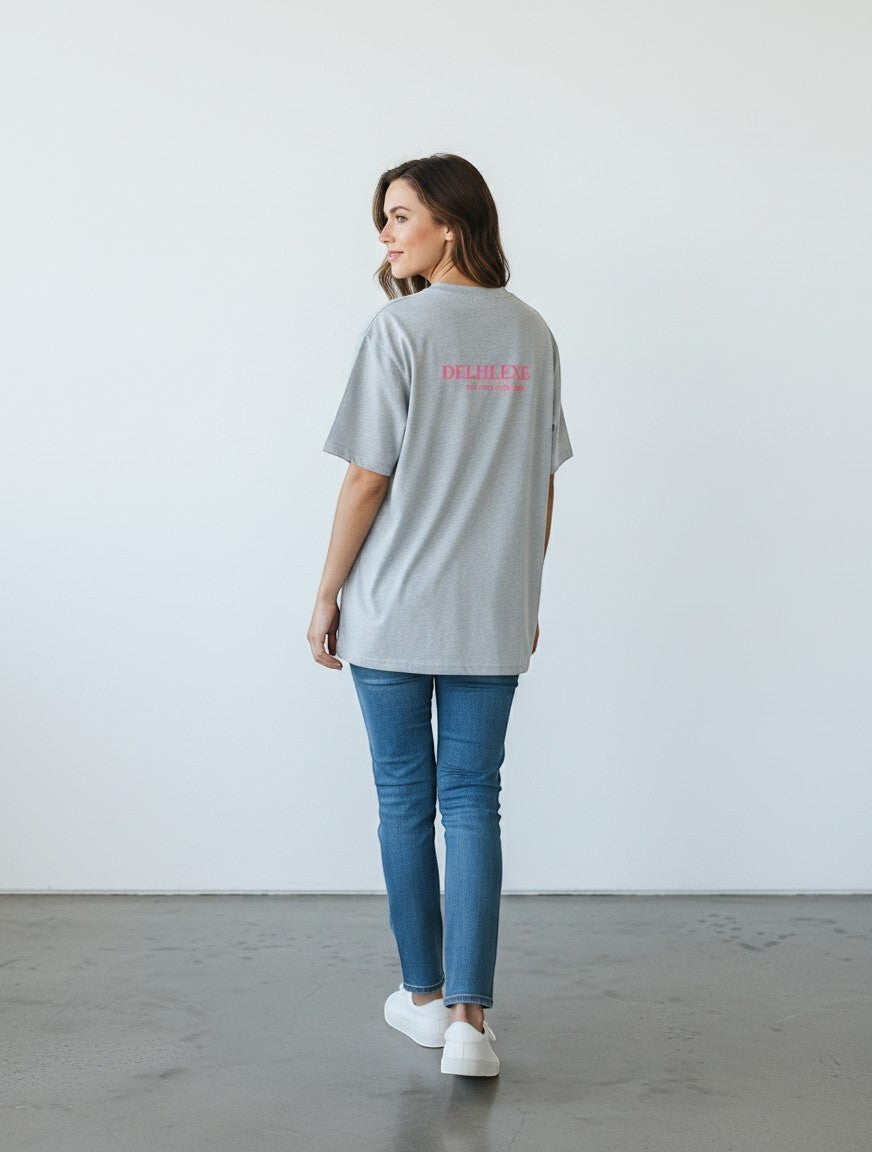 Woman wearing a grey mi-DONE oversized cotton t-shirt with Delhi print on the back, paired with blue jeans and sneakers.