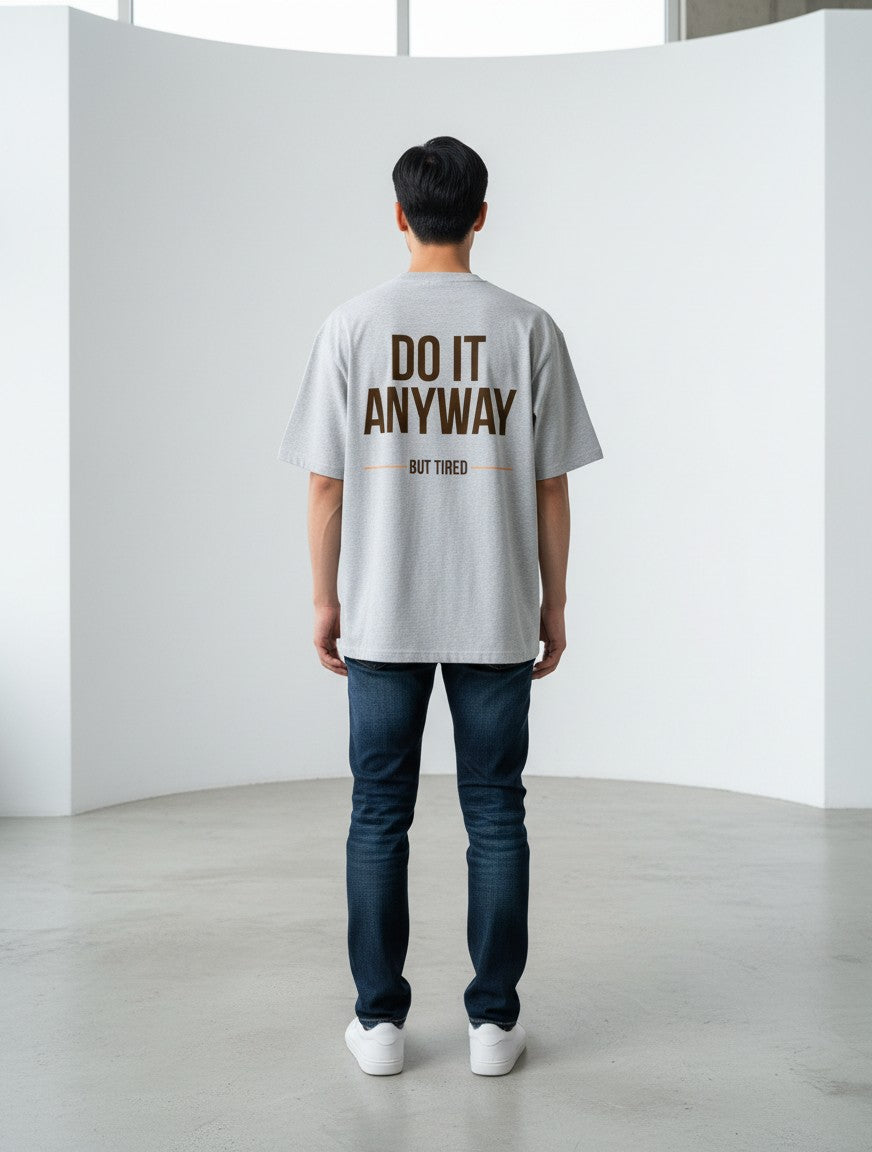 mi-DONE grey oversized cotton t-shirt with Do It Anyway But Tired graphic print on back, worn by a man with jeans