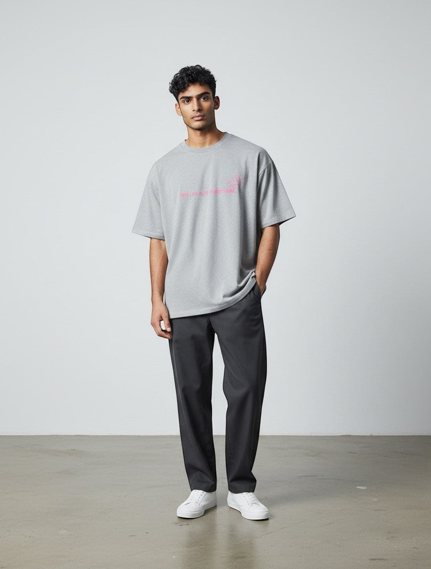 A model wearing a grey mi-DONE oversized cotton t-shirt with a pink graphic print, paired with dark trousers.