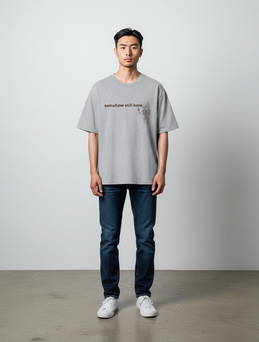 mi-DONE grey oversized cotton t-shirt with skeleton graphic and text on chest worn by a man with dark blue jeans