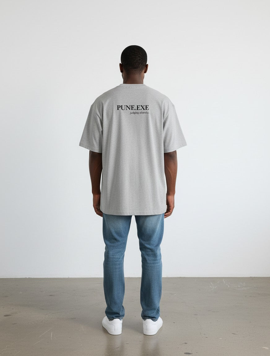 Back view of a man wearing a grey mi-DONE oversized cotton t-shirt with PUNE.EXE print, paired with blue jeans.