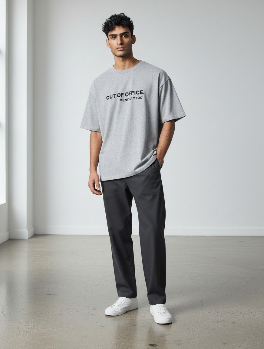 A man wearing a grey mi-DONE oversized cotton t-shirt with Out of Office print, paired with dark trousers.