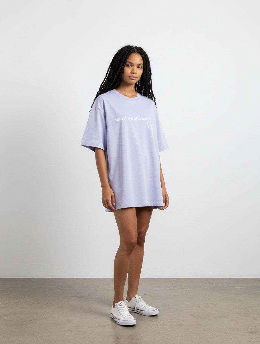 Model wearing a mi-DONE lavender oversized cotton t-shirt with drop shoulders and graphic print, paired with white sneakers.
