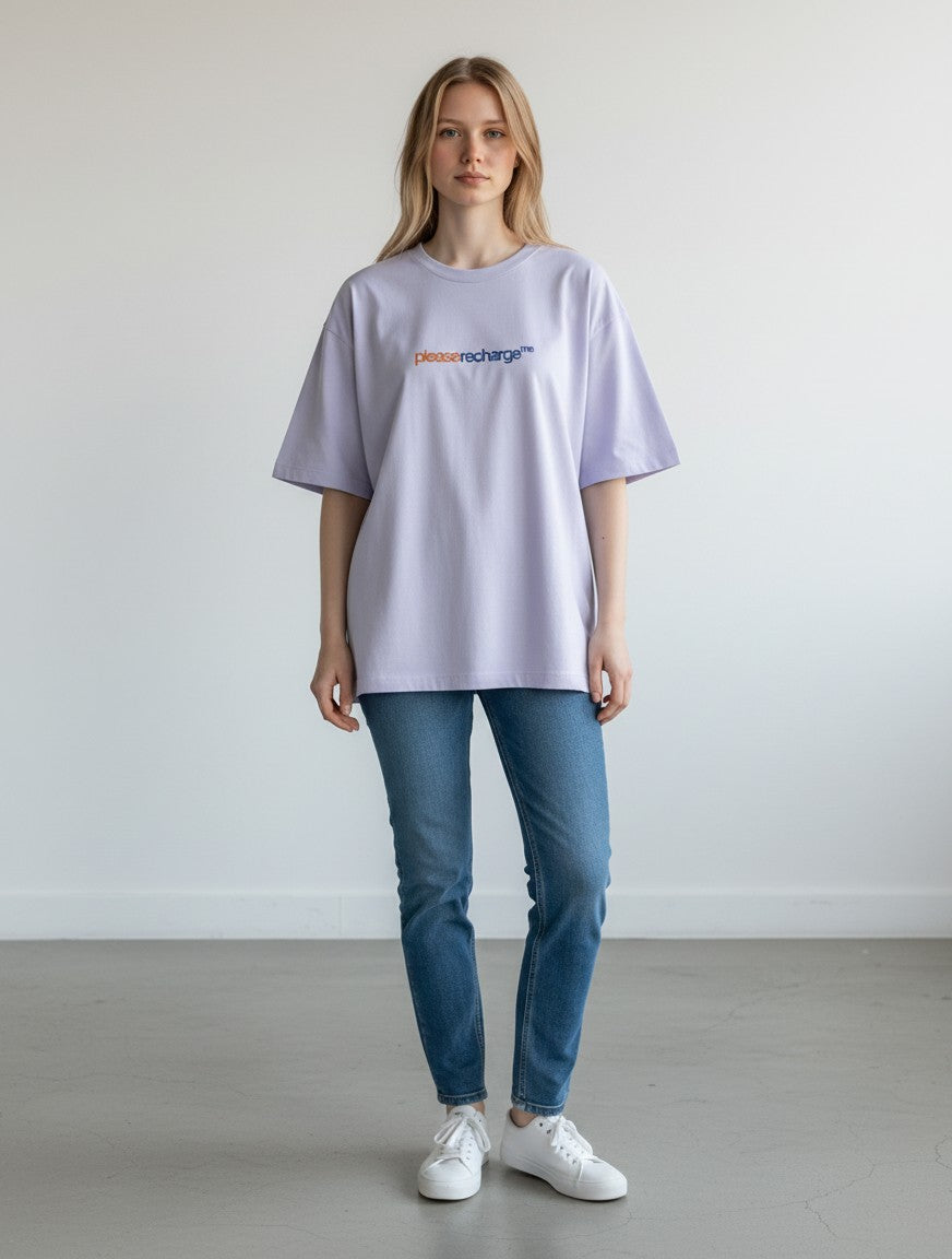 A woman wearing a mi-DONE oversized lilac cotton t-shirt with please recharge me text, paired with blue jeans.