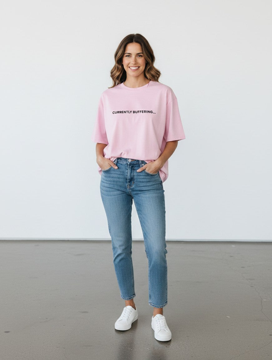 A woman wearing a mi-DONE oversized pink cotton t-shirt with Currently Buffering text, paired with blue jeans.