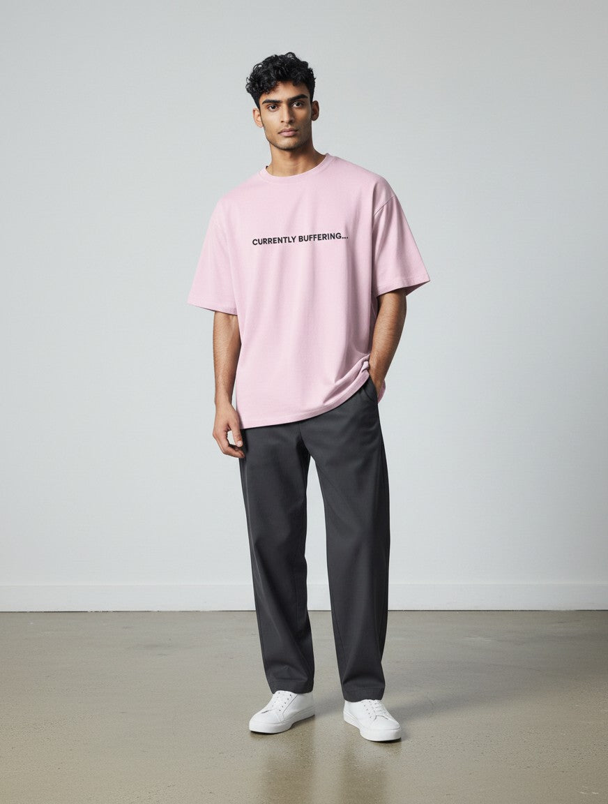 A male model wearing a mi-DONE oversized light pink cotton t-shirt with Currently Buffering text and dark trousers.