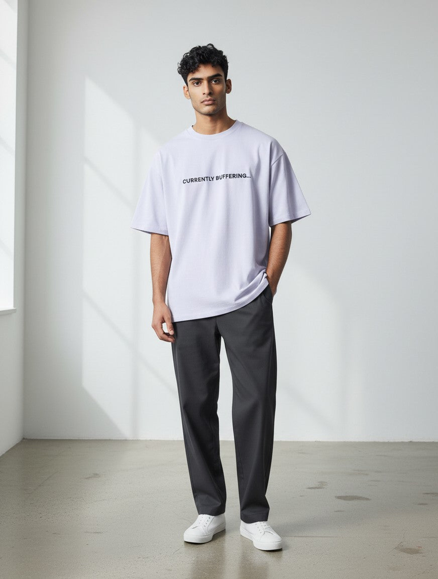 A male model wearing a light purple mi-DONE oversized cotton t-shirt with Currently Buffering text, paired with dark trousers.