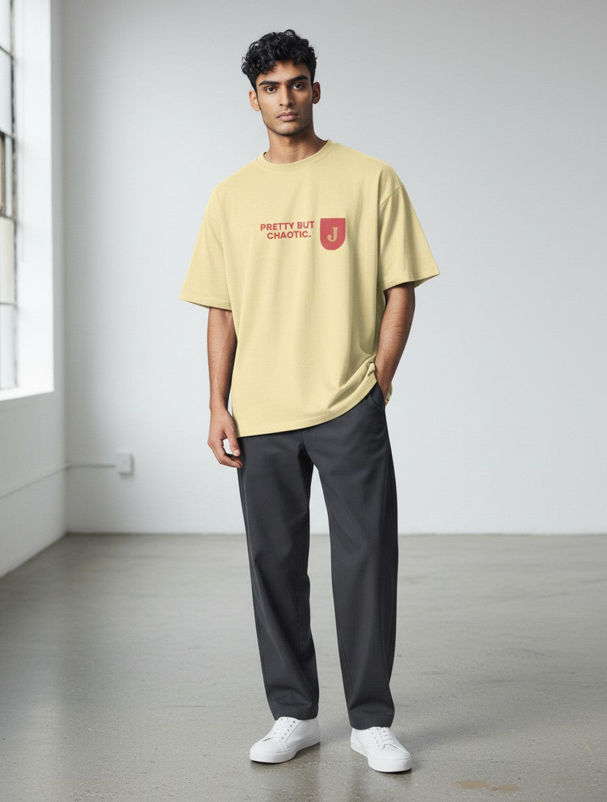 A man wearing a mi-DONE oversized pale yellow cotton t-shirt with Pretty But Chaotic text print and drop shoulders.