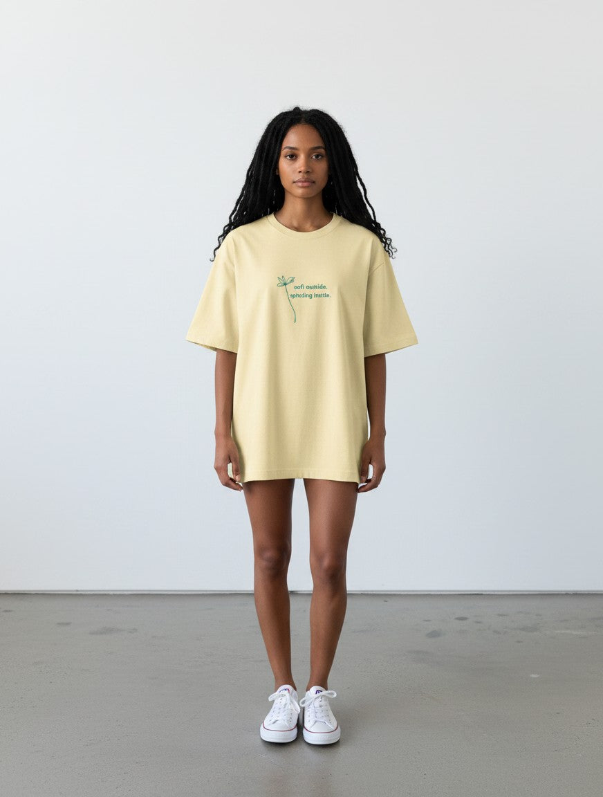 mi-DONE oversized pale yellow cotton t-shirt with green text graphic worn by a woman with long dark hair
