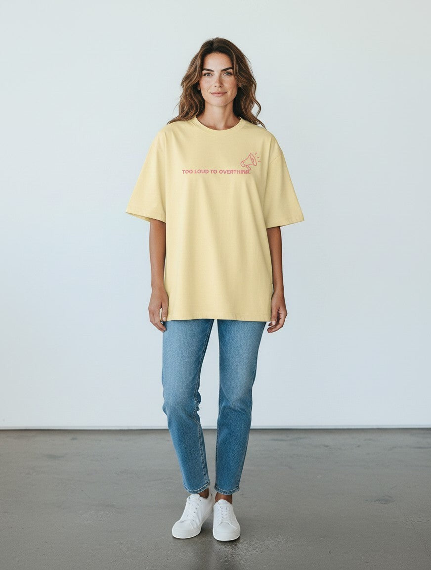 A woman wearing a mi-DONE oversized yellow cotton t-shirt with a graphic print, paired with blue jeans and white sneakers.