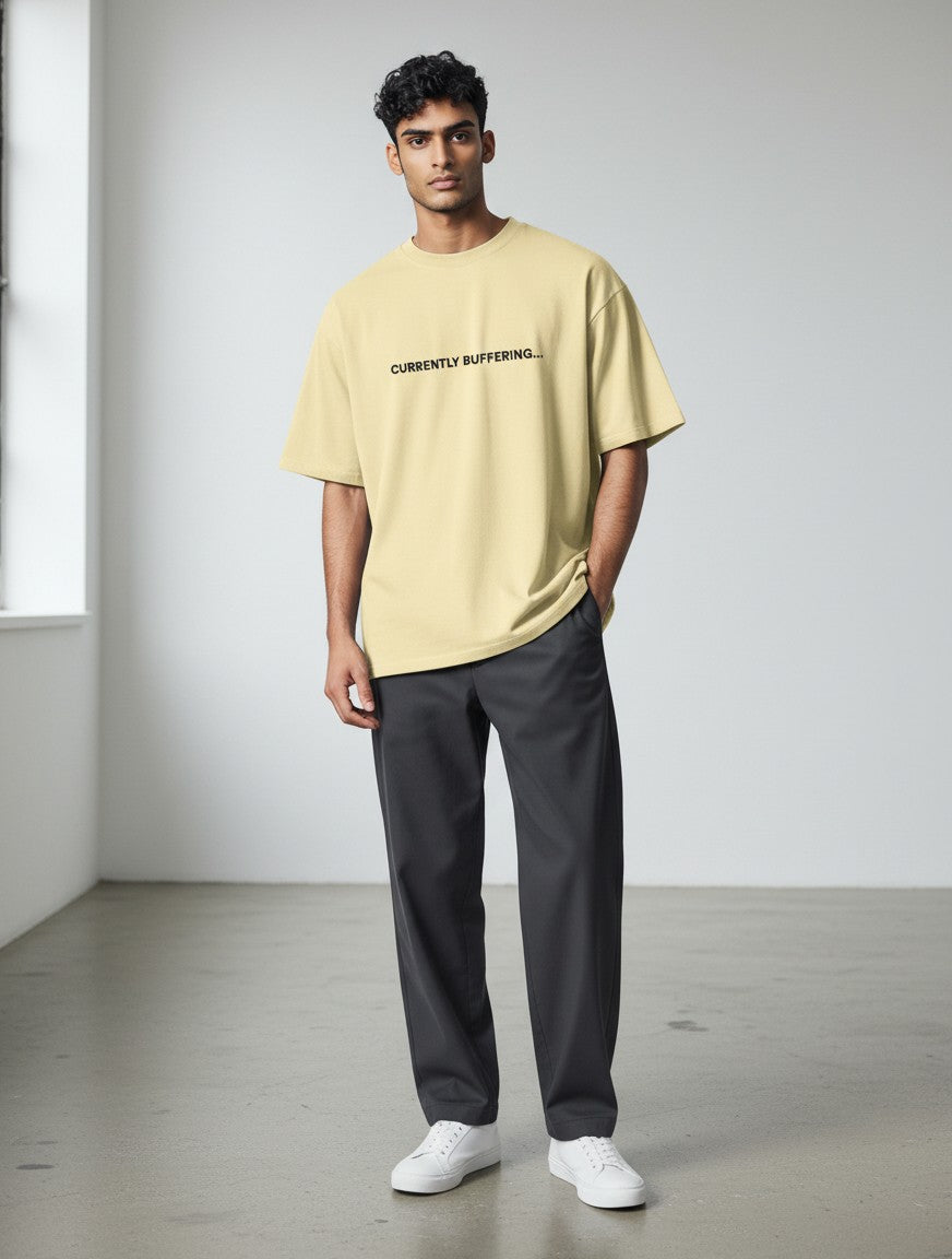 A man wearing a mi-DONE oversized yellow cotton t-shirt with Currently Buffering text, paired with dark trousers.