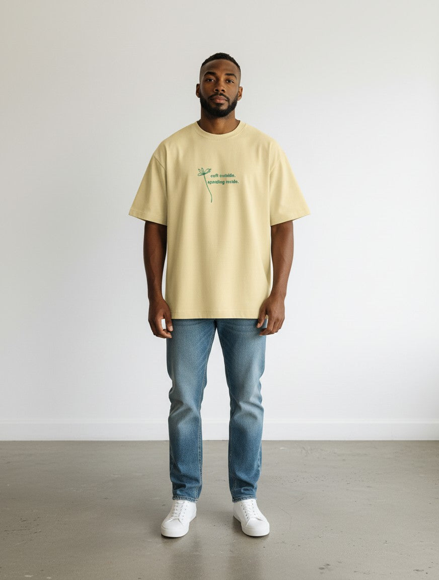 mi-DONE oversized pale yellow cotton t-shirt with green graphic text on chest, worn by a man with blue jeans