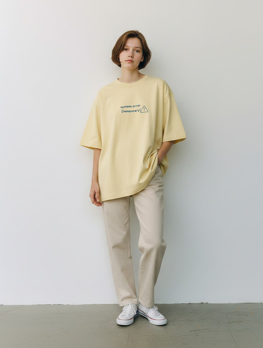 mi-DONE oversized yellow cotton t-shirt with System Error graphic, worn by a woman with beige trousers and sneakers.