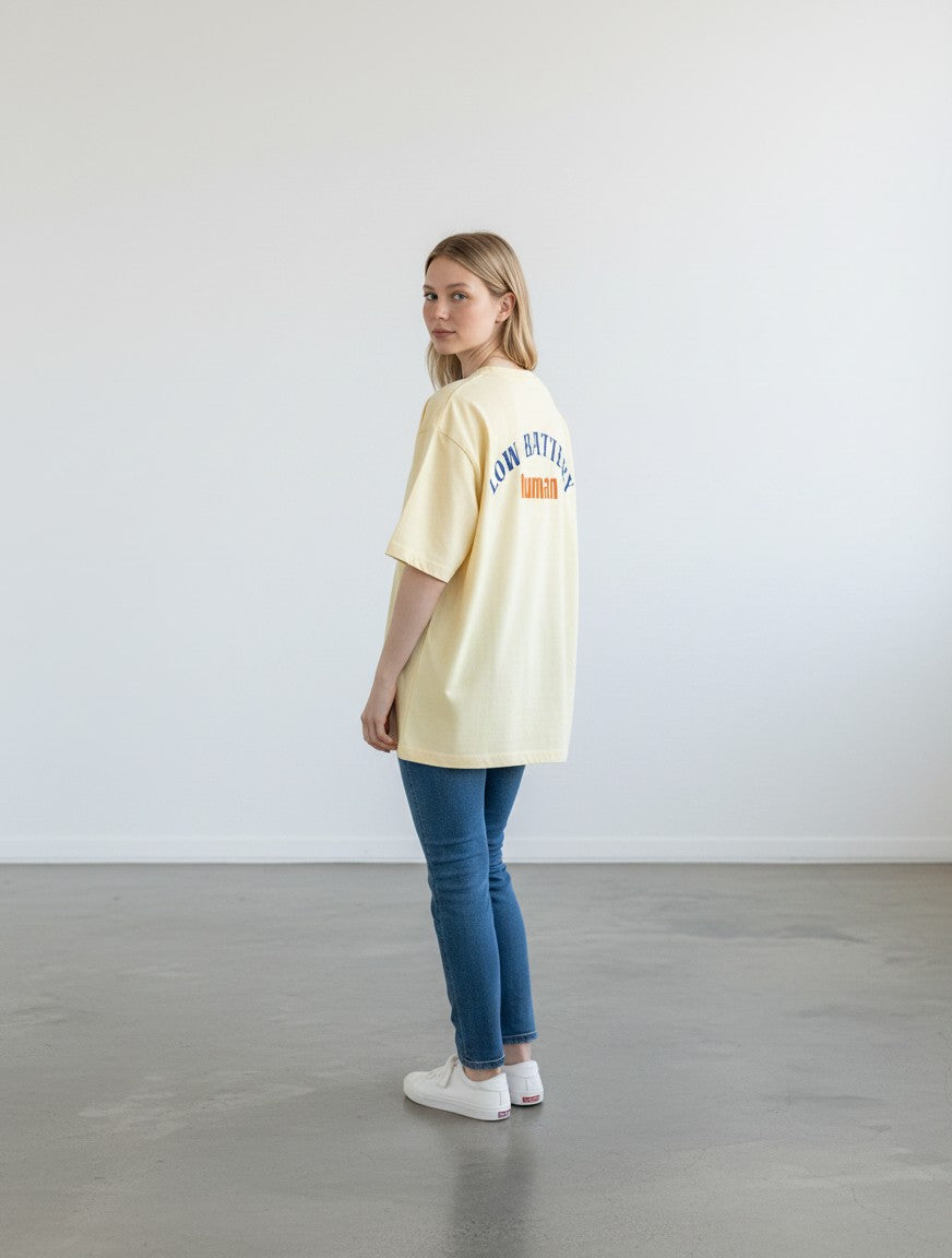 mi-DONE oversized yellow cotton t-shirt with Low Battery graphic print on back worn by a woman with blue jeans