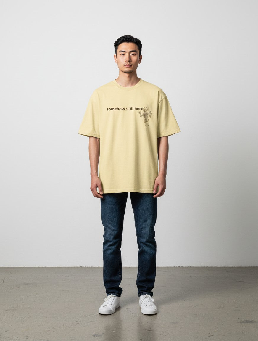 mi-DONE oversized yellow cotton t-shirt with skeleton graphic and somehow still here text on a male model