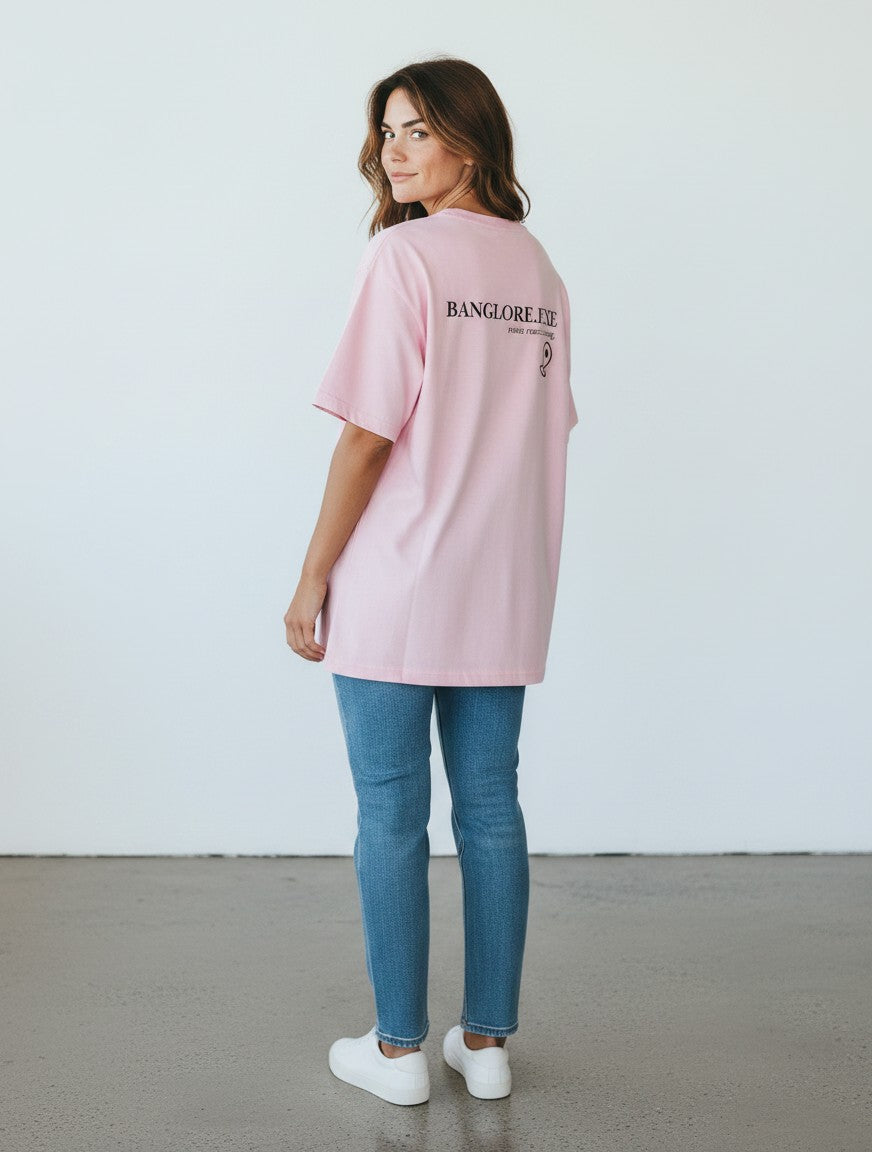 A woman wearing a pink mi-DONE oversized cotton t-shirt with Bengaluru graphic print, styled with blue jeans.