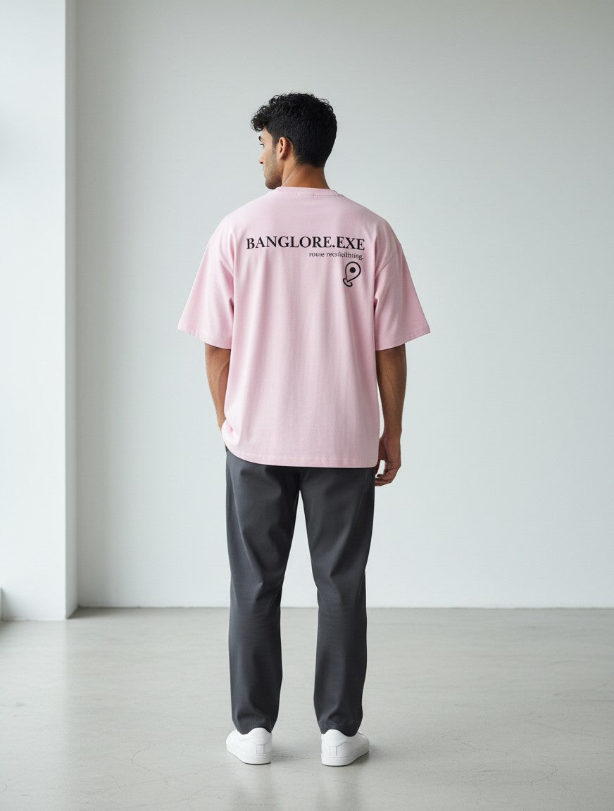 A man wearing a pink mi-DONE oversized cotton t-shirt with a black Banglore.exe graphic on the back, seen from behind.