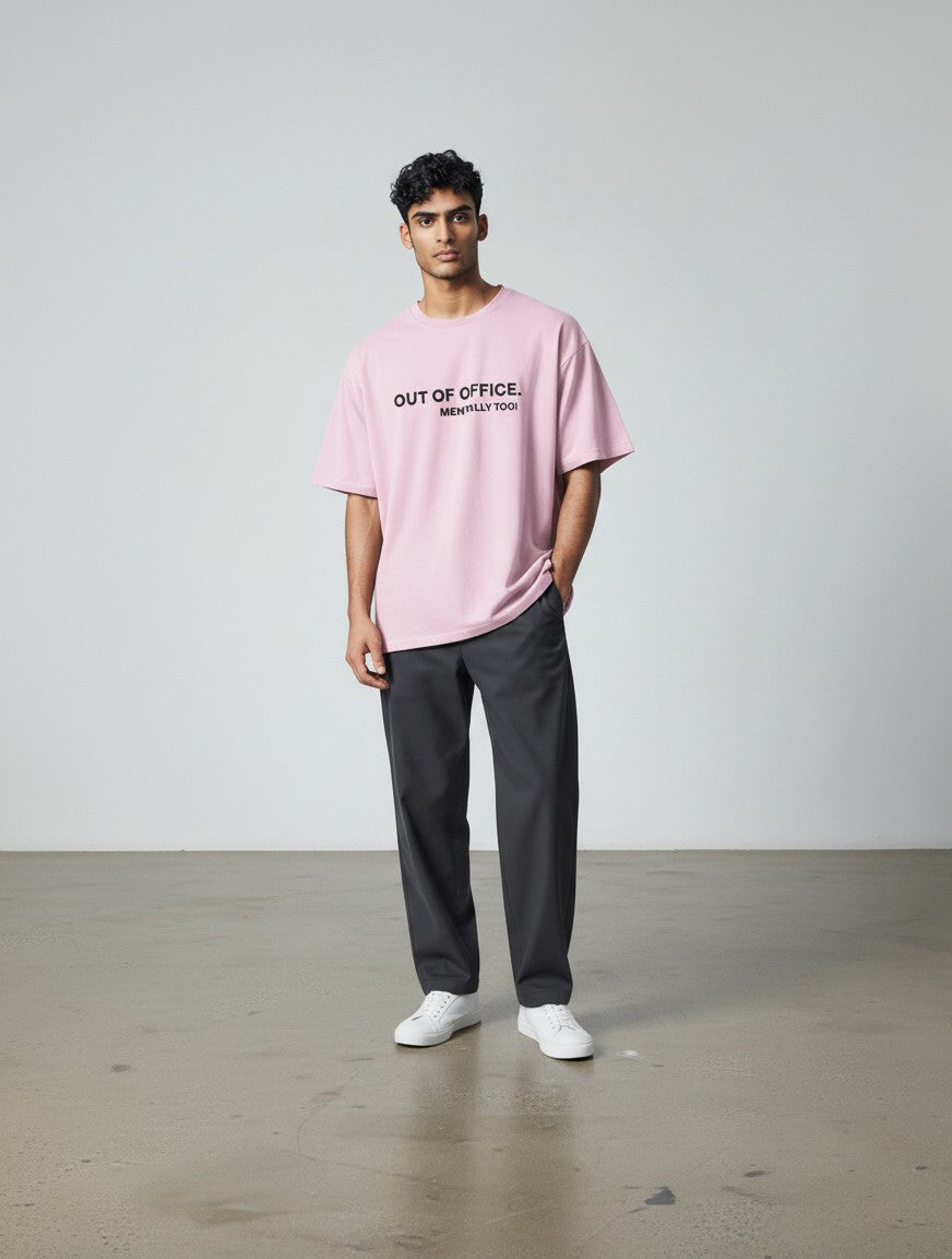 A male model wearing a pink mi-DONE oversized cotton t-shirt with Out of Office text print and dark grey trousers.