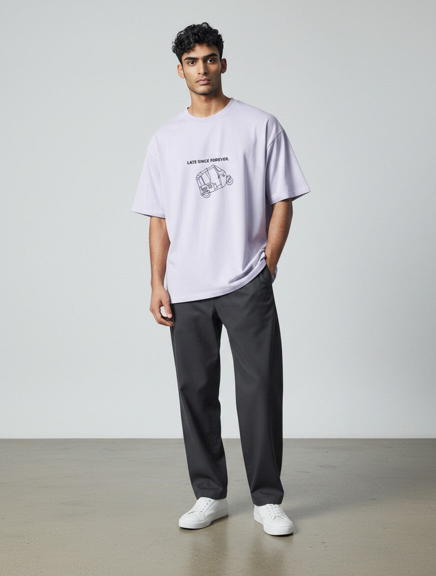 A man wearing a light purple mi-DONE oversized cotton t-shirt with a Mumbai rickshaw graphic and dark grey trousers.