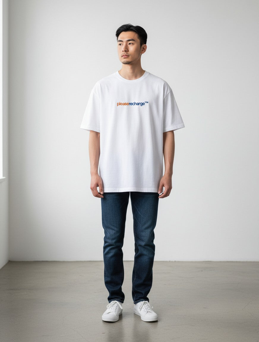 A man wearing a white mi-DONE oversized cotton t-shirt with a please recharge graphic print and dark blue jeans.