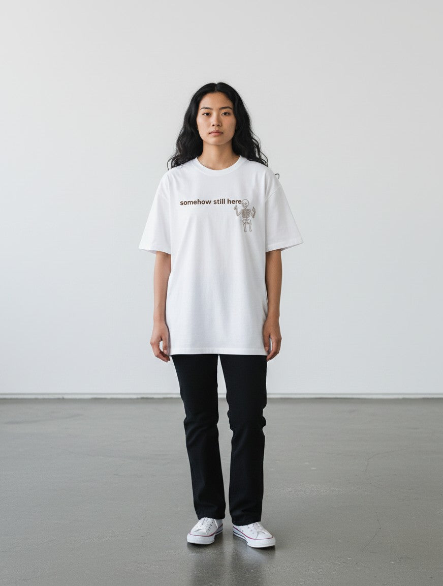 mi-DONE white oversized cotton t-shirt with skeleton graphic and somehow still here text worn by a woman