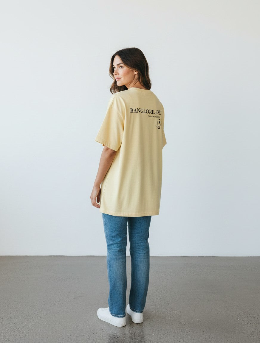 A woman wearing a yellow mi-DONE oversized cotton t-shirt with Bengaluru graphic print, paired with blue jeans.