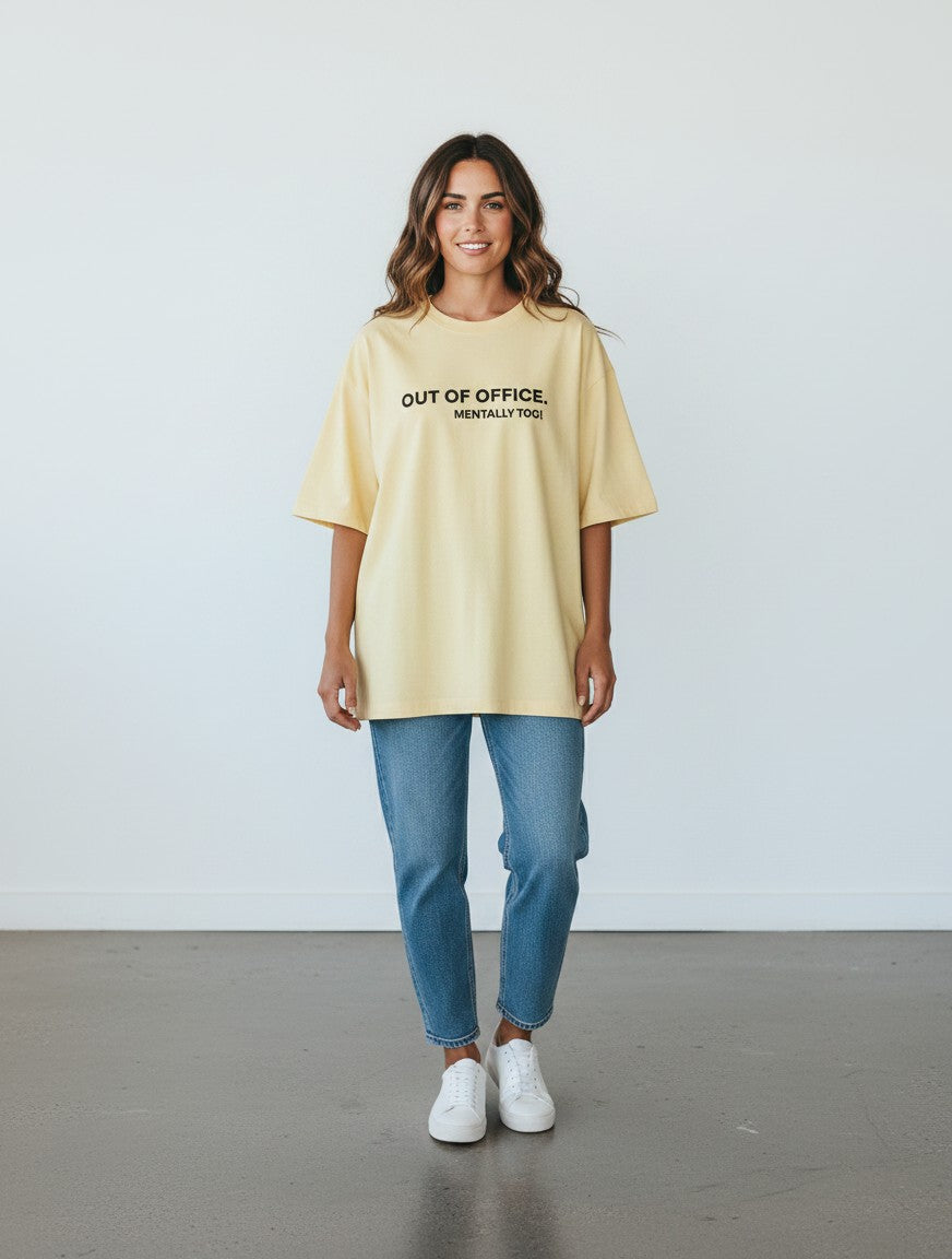 A woman wearing a yellow mi-DONE oversized cotton t-shirt with Out of Office text, paired with blue jeans.