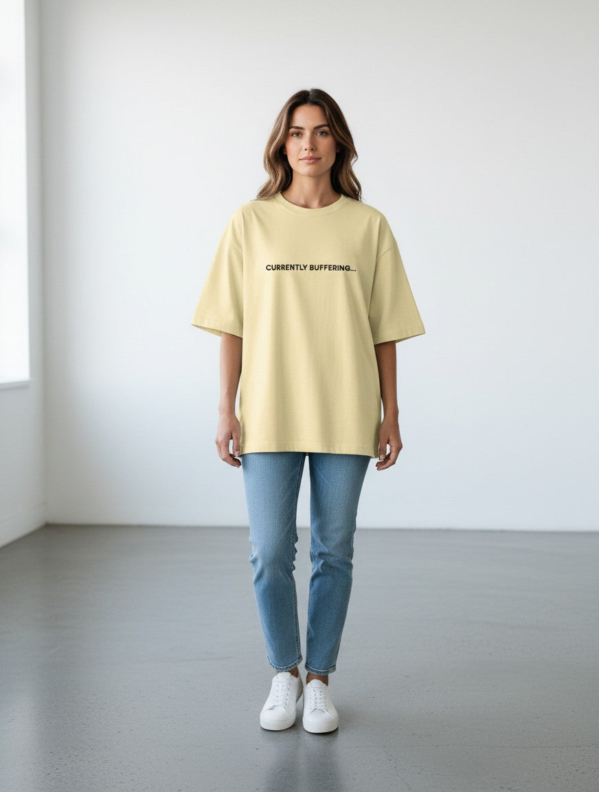 A woman wearing a pale yellow mi-DONE oversized cotton t-shirt with the text Currently Buffering printed on the chest.